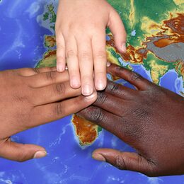 Drei Hände mit verschiedener Hautfarbe berühren sich über einer Weltkarte